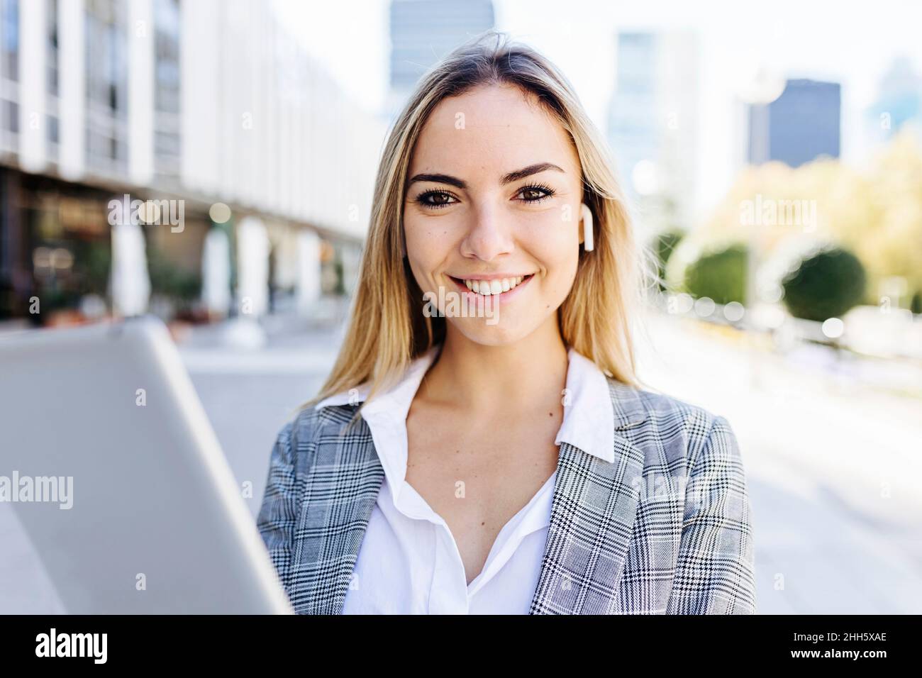 Smiling working woman with tablet PC wearing wireless in-ear headphones Stock Photo