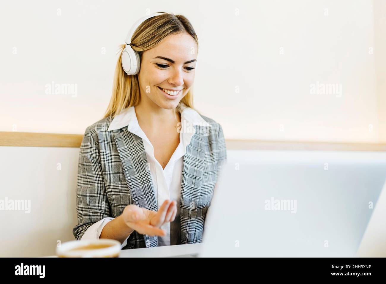 Smiling blond freelancer wearing headphones on video call through ...