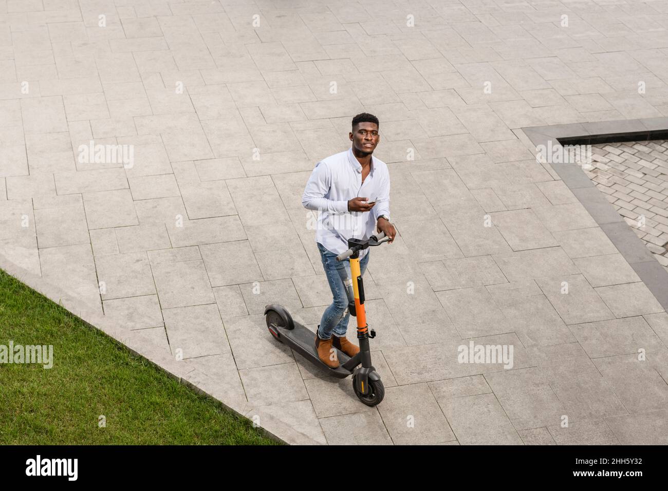 Young man with electric push scooter on footpath Stock Photo