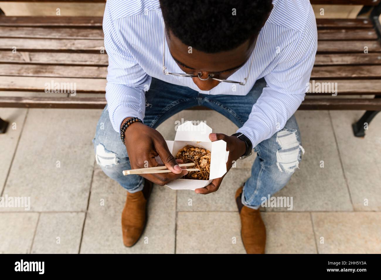 Young man having food sitting on bench Stock Photo