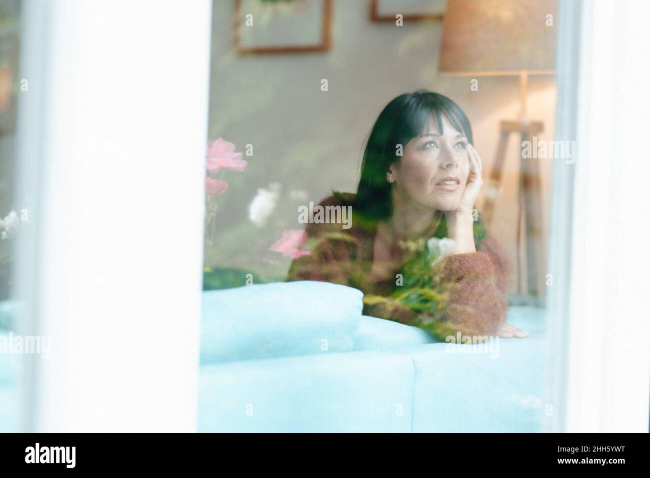 Thoughtful woman looking through window Stock Photo