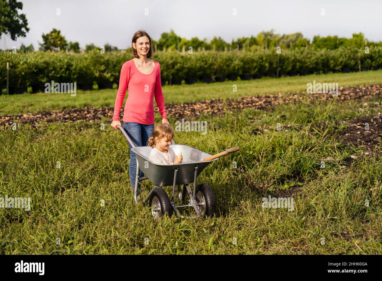 Smiling mother with daughter sitting in wheelbarrow Stock Photo - Alamy