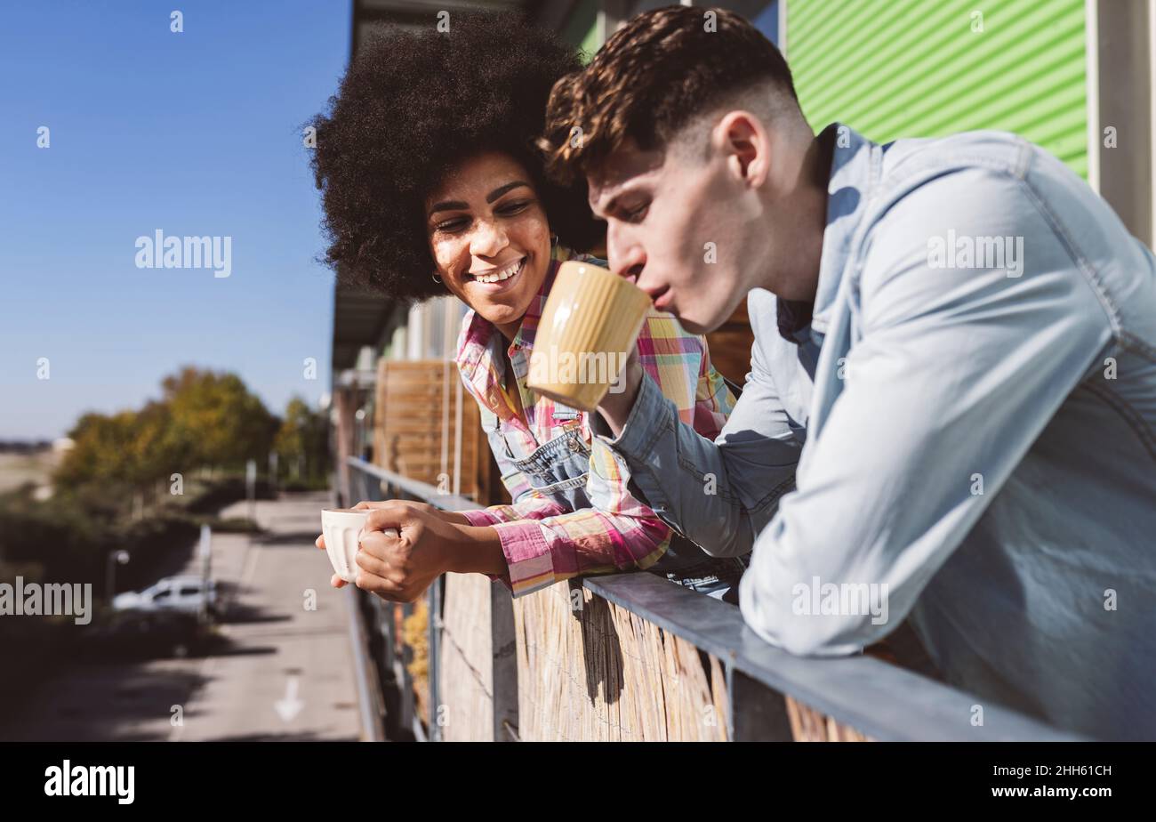 Young couple enjoying coffee together standing on balcony on sunny day Stock Photo