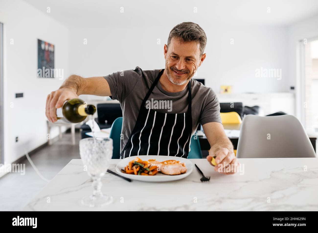 Smiling man pouring wine in glass by meal at table Stock Photo