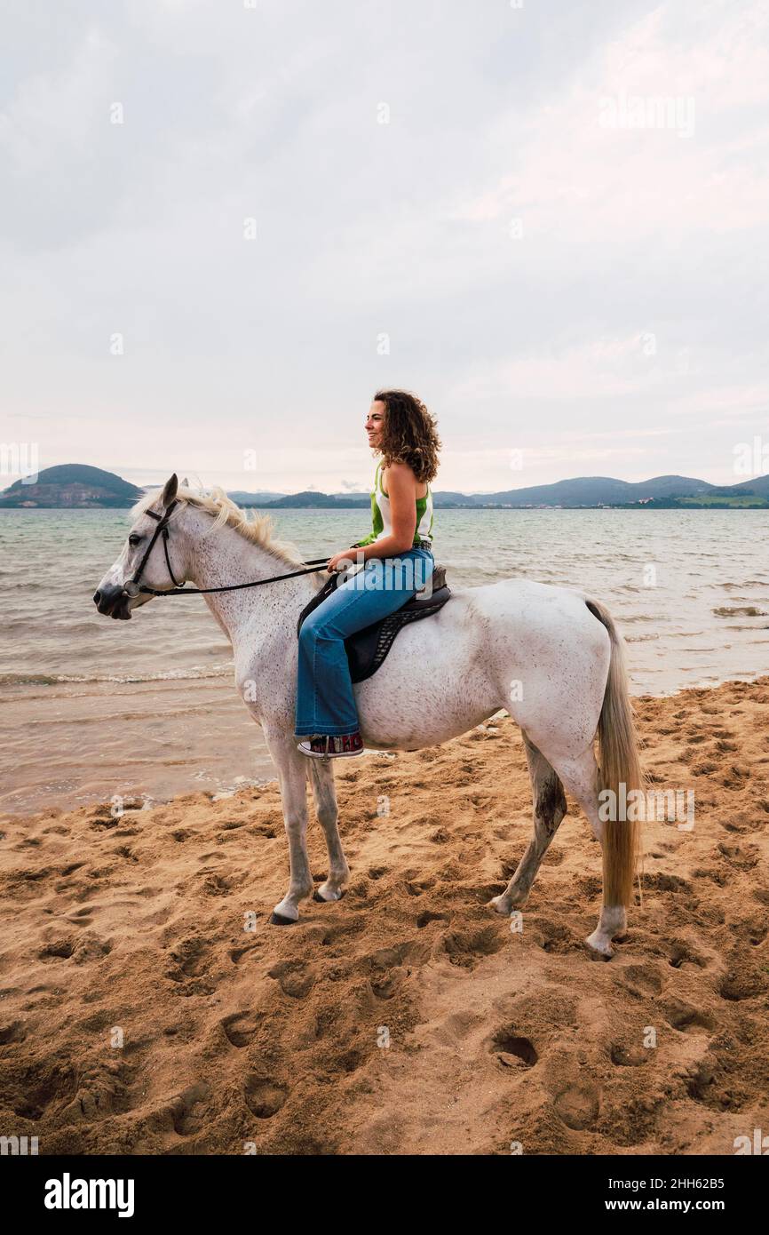 Smiling young woman riding horse at waterfront Stock Photo