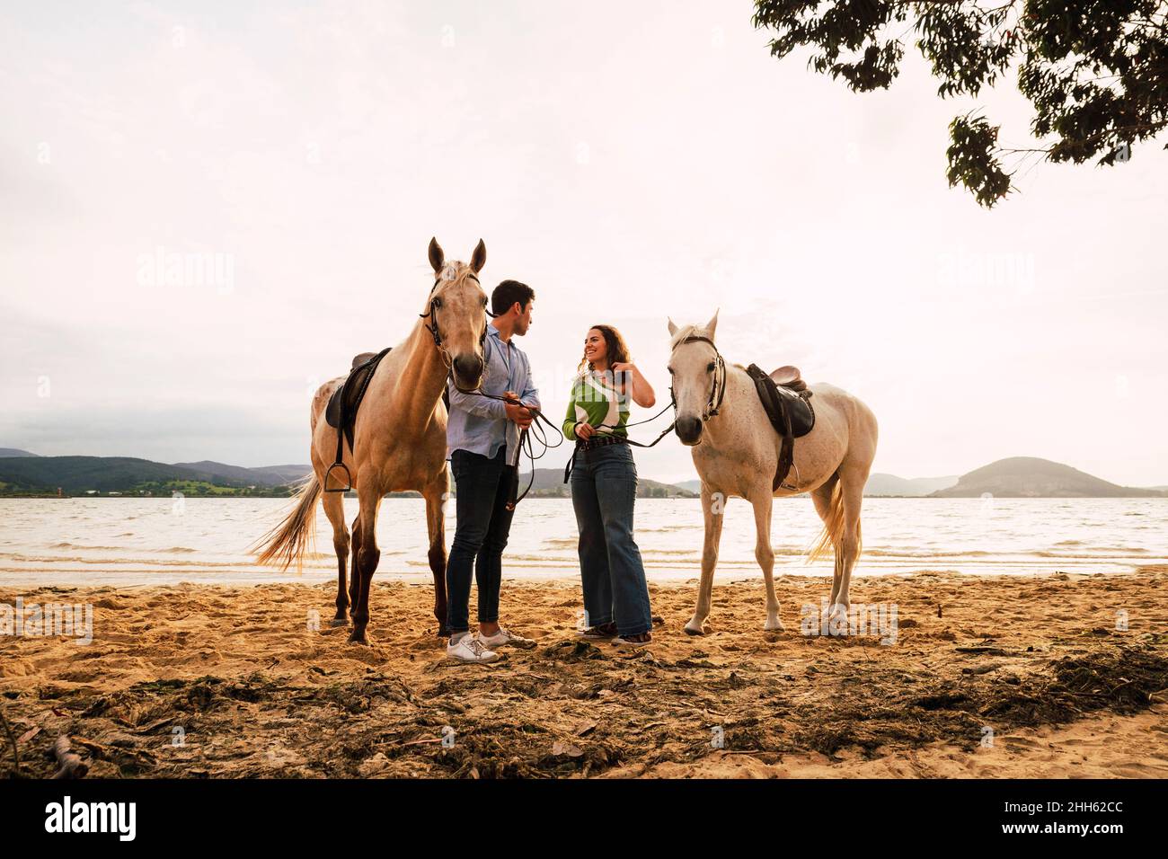 Young man and woman standing with horses at waterfront Stock Photo