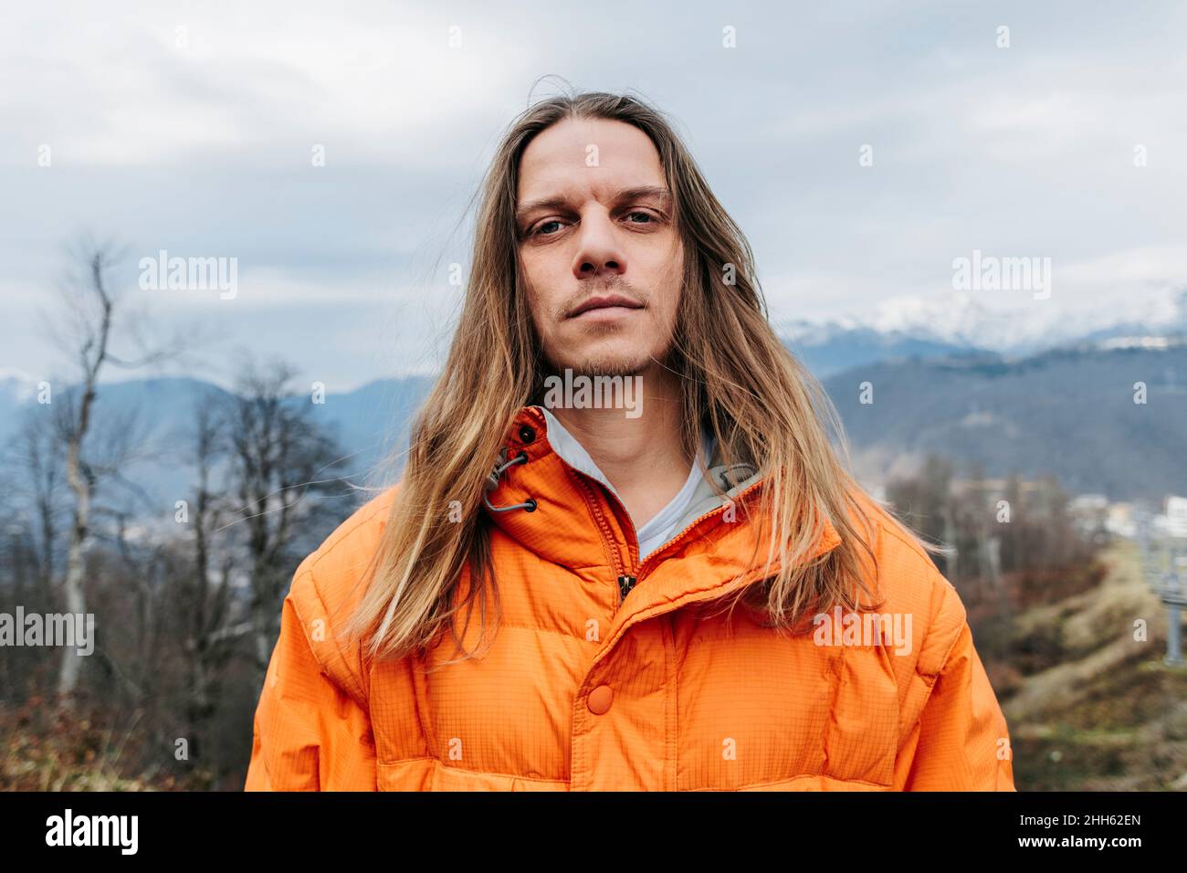 Man with blond long hair wearing orange jacket Stock Photo