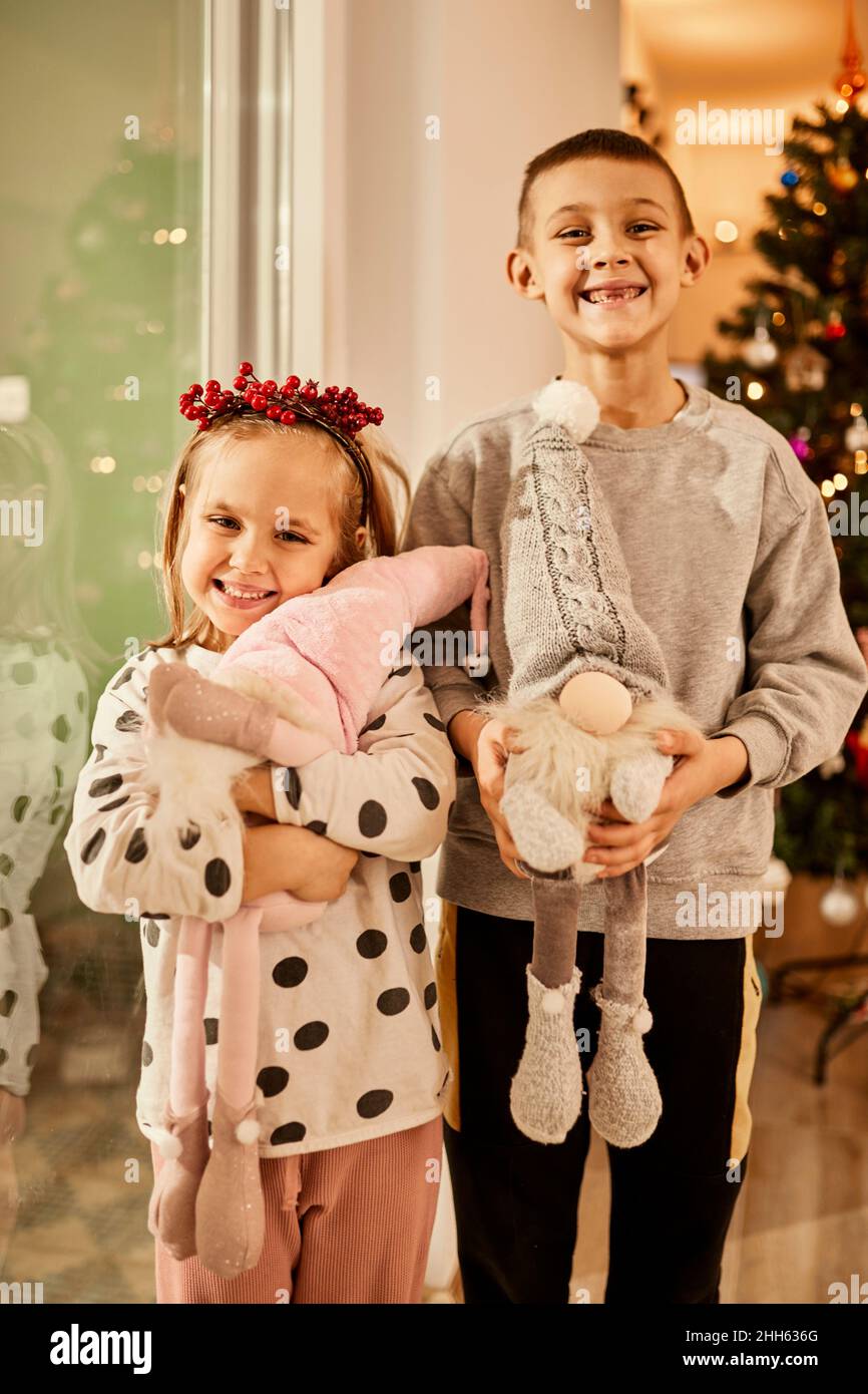 Happy sibling with toy gnomes standing in front of christmas tree at home Stock Photo