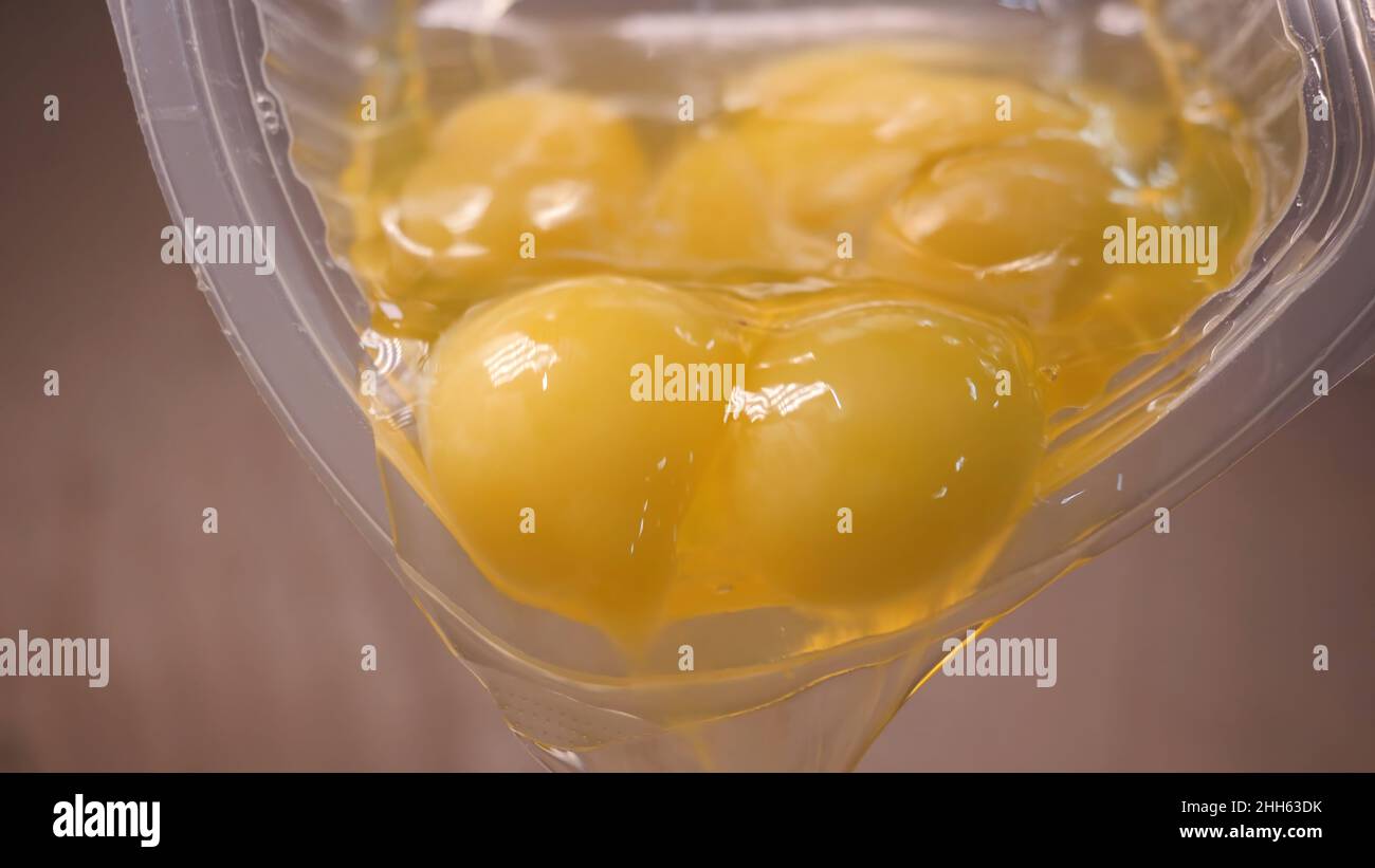Close-up of raw eggs poured from cup. Stock footage. Raw eggs with yolks and proteins spread from plastic container for baking. Stock Photo