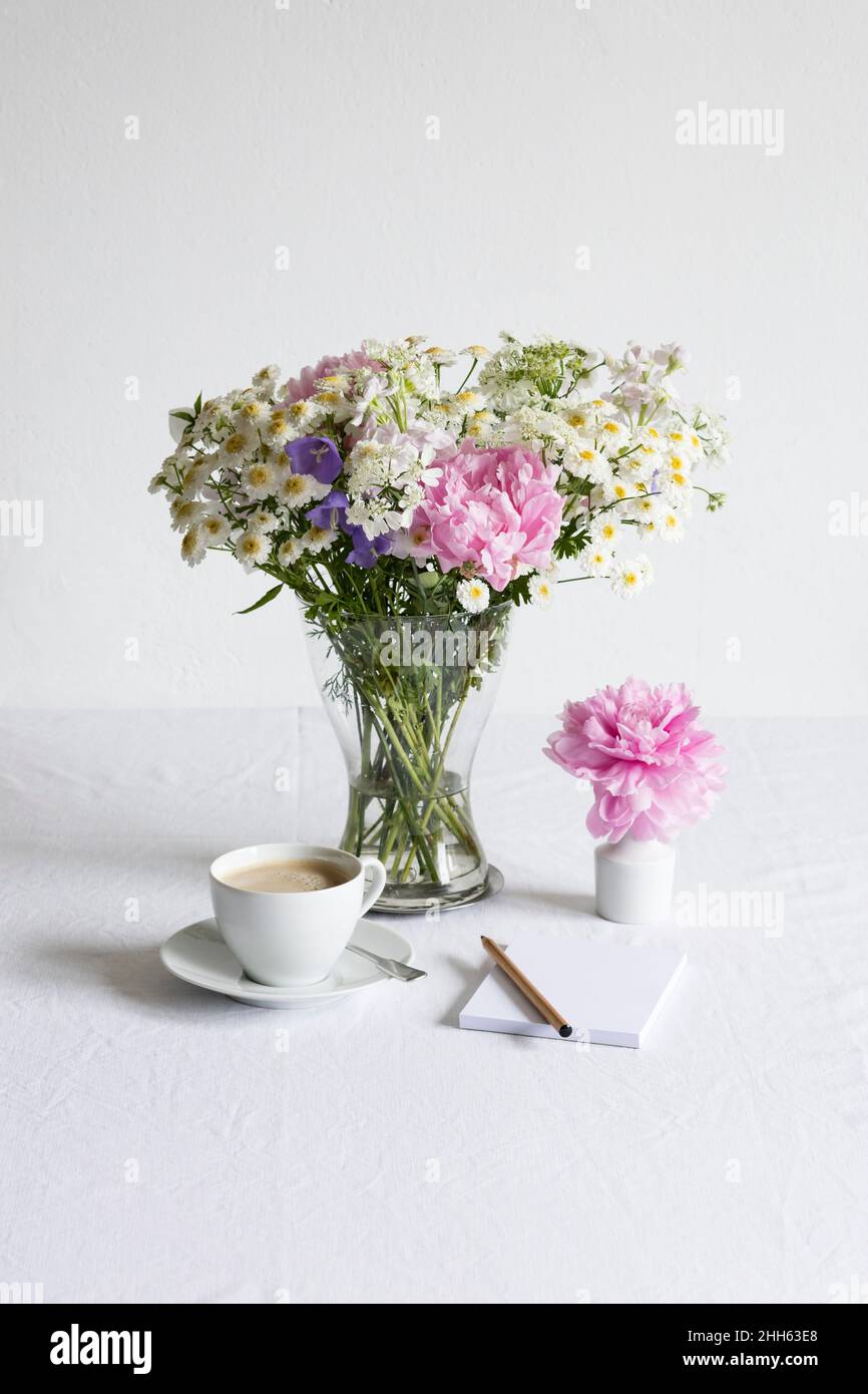 Studio shot of cup of coffee and bouquet of peonies, feverfews (Tanacetum parthenium), bellflowers (Campanula) and white laceflowers (Orlaya grandiflora) Stock Photo