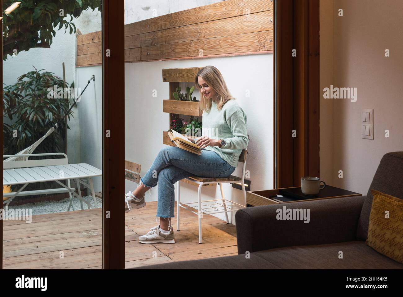 Woman reading book sitting on chair at patio Stock Photo - Alamy