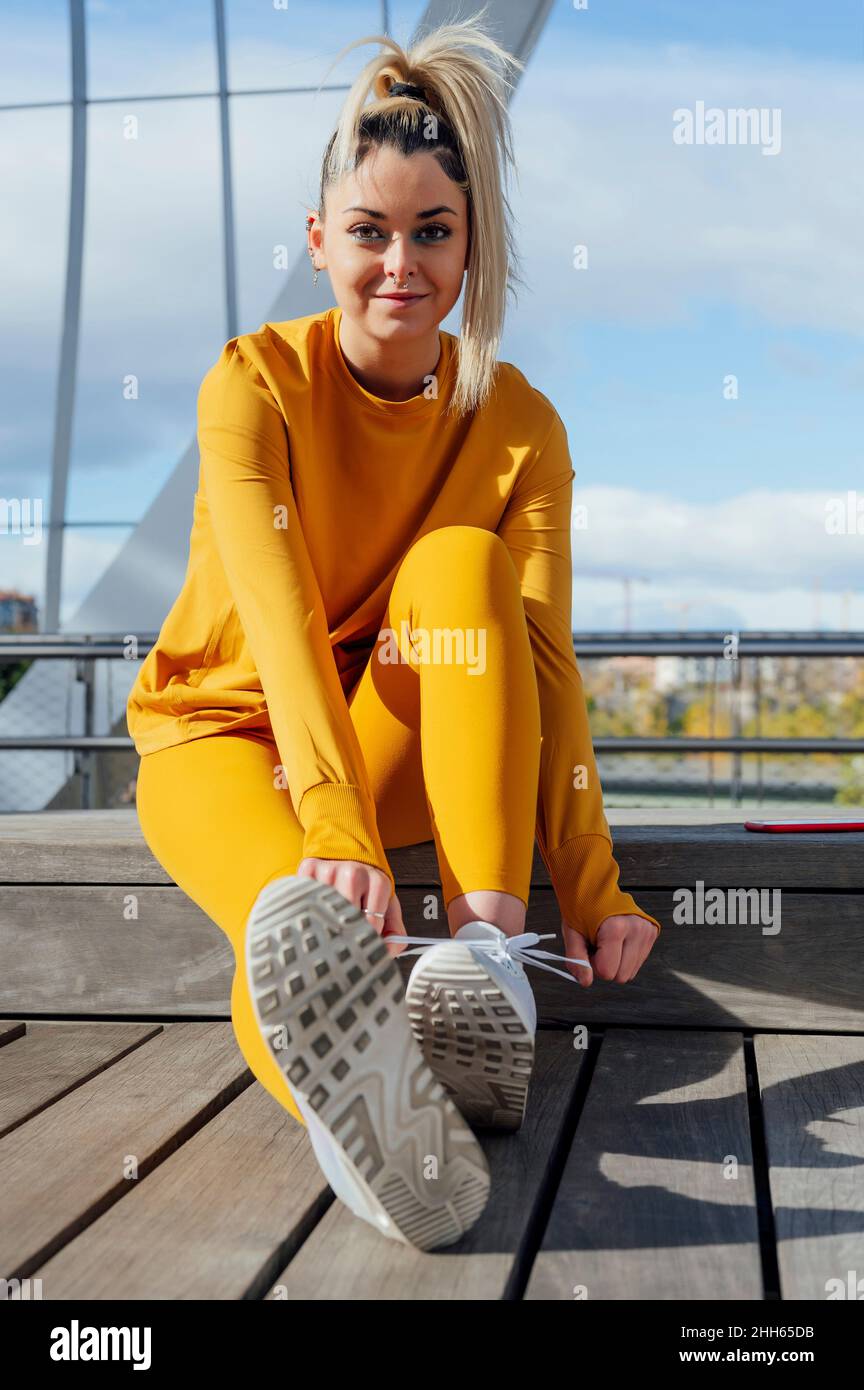 Beautiful young sportswoman tying shoelace sitting on bridge Stock Photo