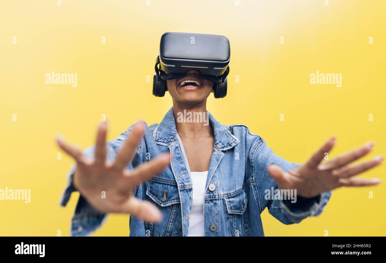 Smiling young woman wearing virtual reality headset gesturing against ...