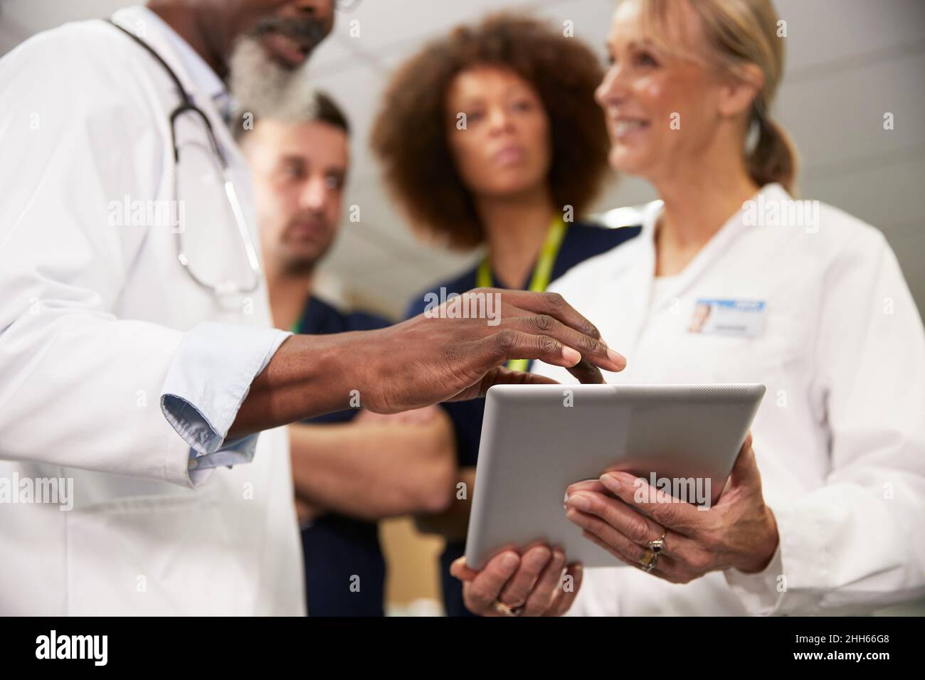 Doctor using tablet PC with colleagues in meeting at hospital Stock Photo