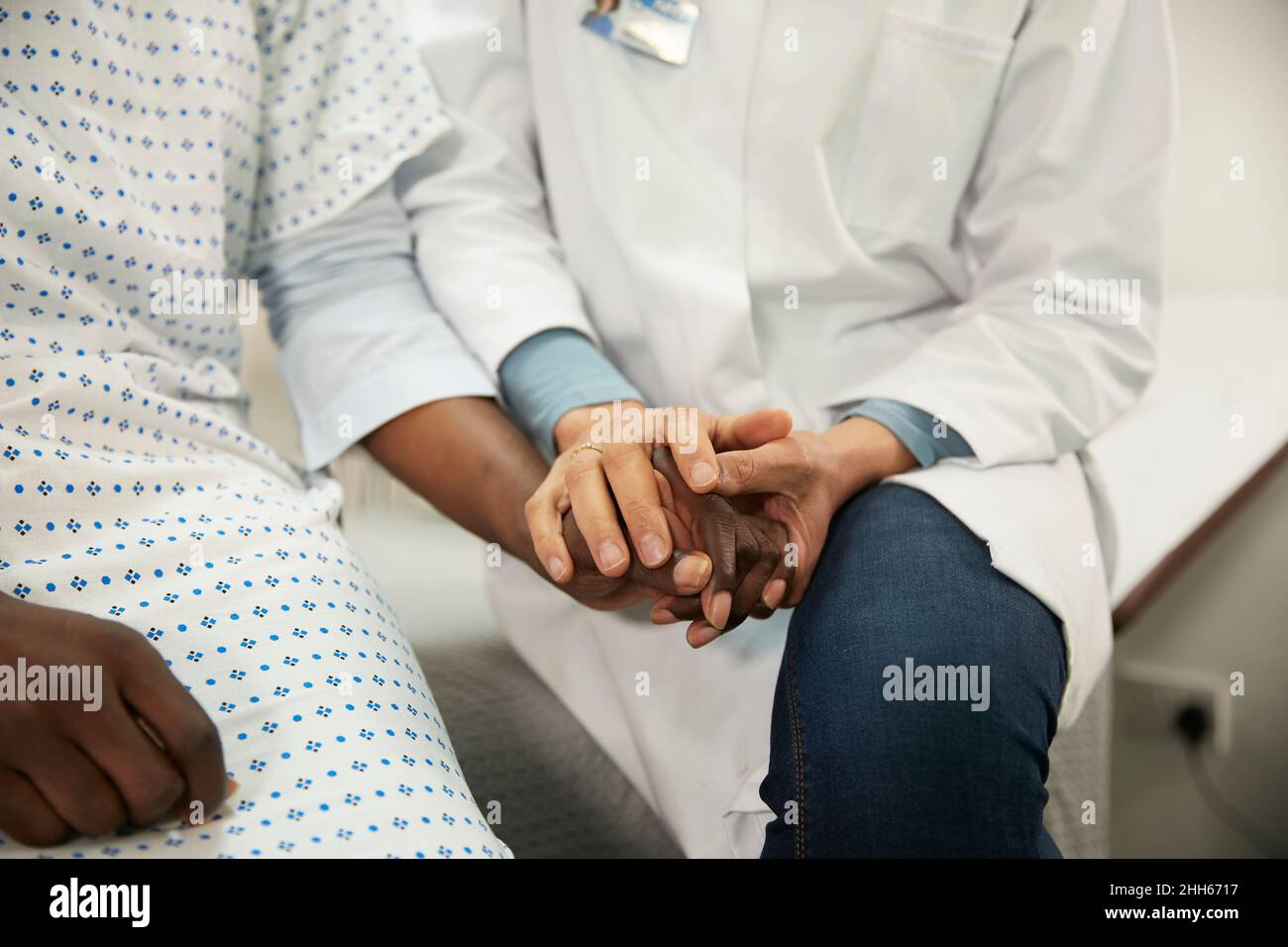 Doctor holding hands and consoling patient in medical room Stock Photo