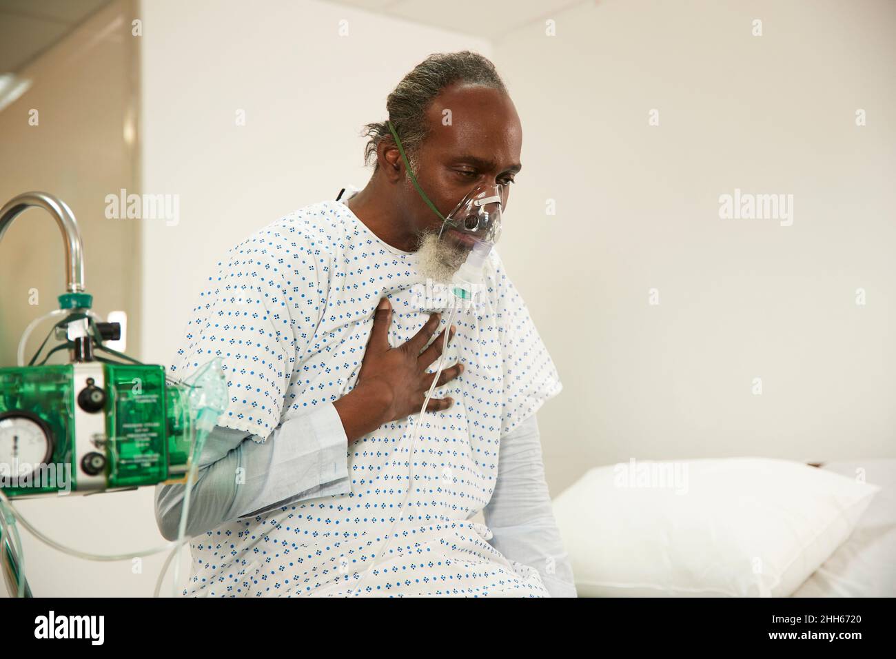 Patient touching chest wearing oxygen mask in medical room Stock Photo