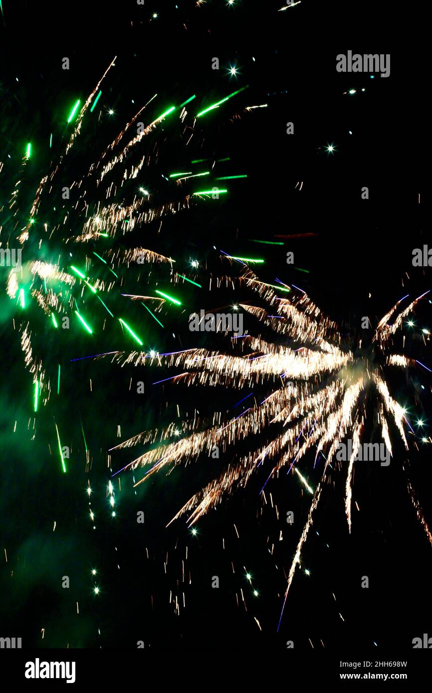 Green and yellow fireworks exploding against clear night sky Stock Photo