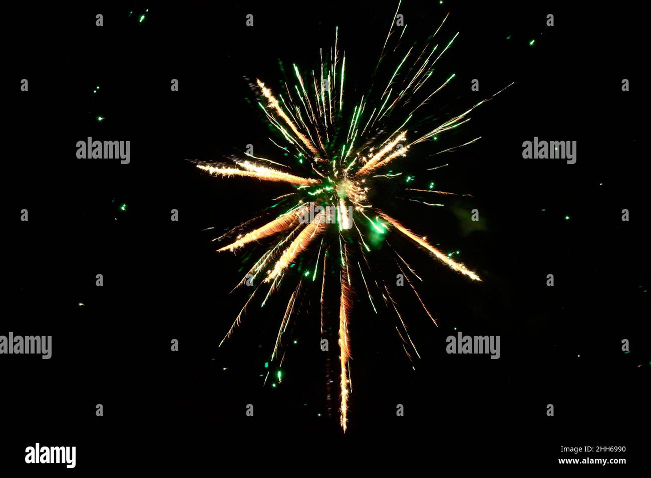 Green and yellow fireworks exploding against clear night sky Stock Photo