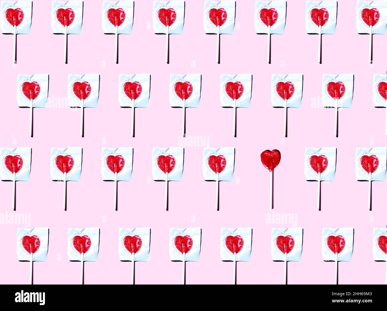 Pattern of heart shaped lollipops flat laid against pink background with single one unwrapped Stock Photo