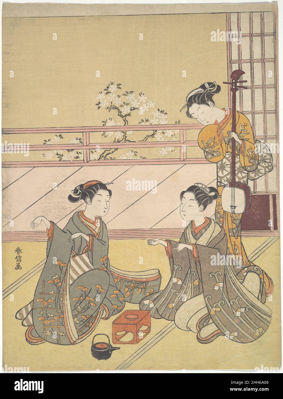 Young Women Playing Kitsune-ken (Fox Game) ca. 1768–69 Suzuki Harunobu Japanese The spaciousness of the interior in this print extends to the exterior space of the veranda and the blossoming cherry trees beyond the railing, creating a pleasant atmosphere. The joyous mood is echoed by two figures in the foreground playing the fox game (kitsune-ken). Another young woman, with a three-stringed samisen in her left hand, watches their game. On the floor between the contestants are a kettle and a stand holding a sake cup.The basic idea of kitsune-ken is that three hand gestures symbolize a village c Stock Photo