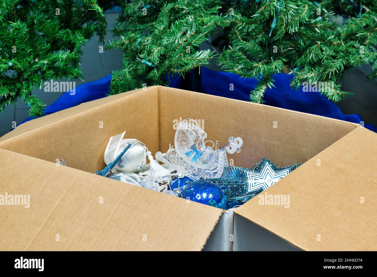 Packing away Christmas decorations after the new year. Box of ornaments in front of empty tree and skirt. Stock Photo