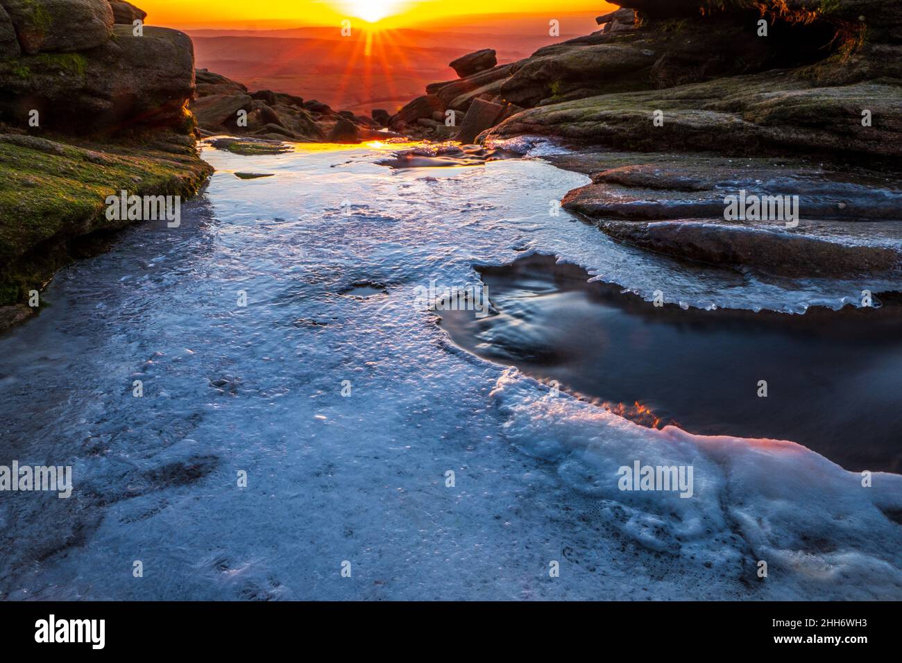 Ice on The river Kinder at Kinder Downfall in the Peak District, setting sun in the distance Stock Photo