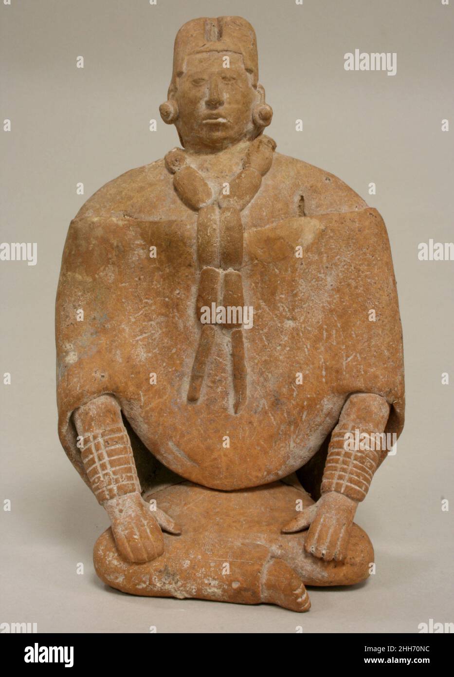 Seated Female Figure 6th–9th century Maya In the form of a seated royal Maya woman, this figurine also probably functioned as a whistle, with the mouthpiece cleverly hidden in the coiffure of the subject and an opening on the figure’s right shoulder. The woman crosses her legs which are covered by a long skirt. Her hands rest on her shins and she wears cuffs composed of tubular beads, likely depicting jadeite or greenstone. Other jade ornaments are depicted, including an earflare assemblage (see 1989.314.15a, b). She wears a long necklace that may be composed of fine cloth or leather with tubu Stock Photo