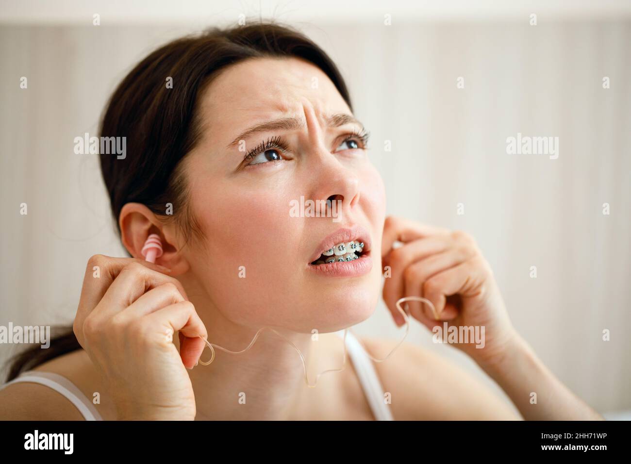 The woman covers her ears because of the loud noise. Noisy neighbors listen to loud music and interfere with sleep. Using earplugs. Stock Photo