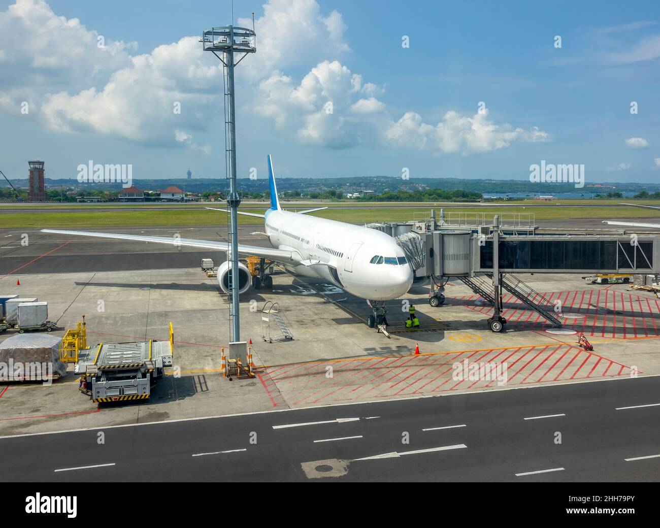 Sunny day at the Indonesian airport. An aircraft with an attached jet bridge for boarding and disembarking passengers. Ocean and jungle in the backgro Stock Photo