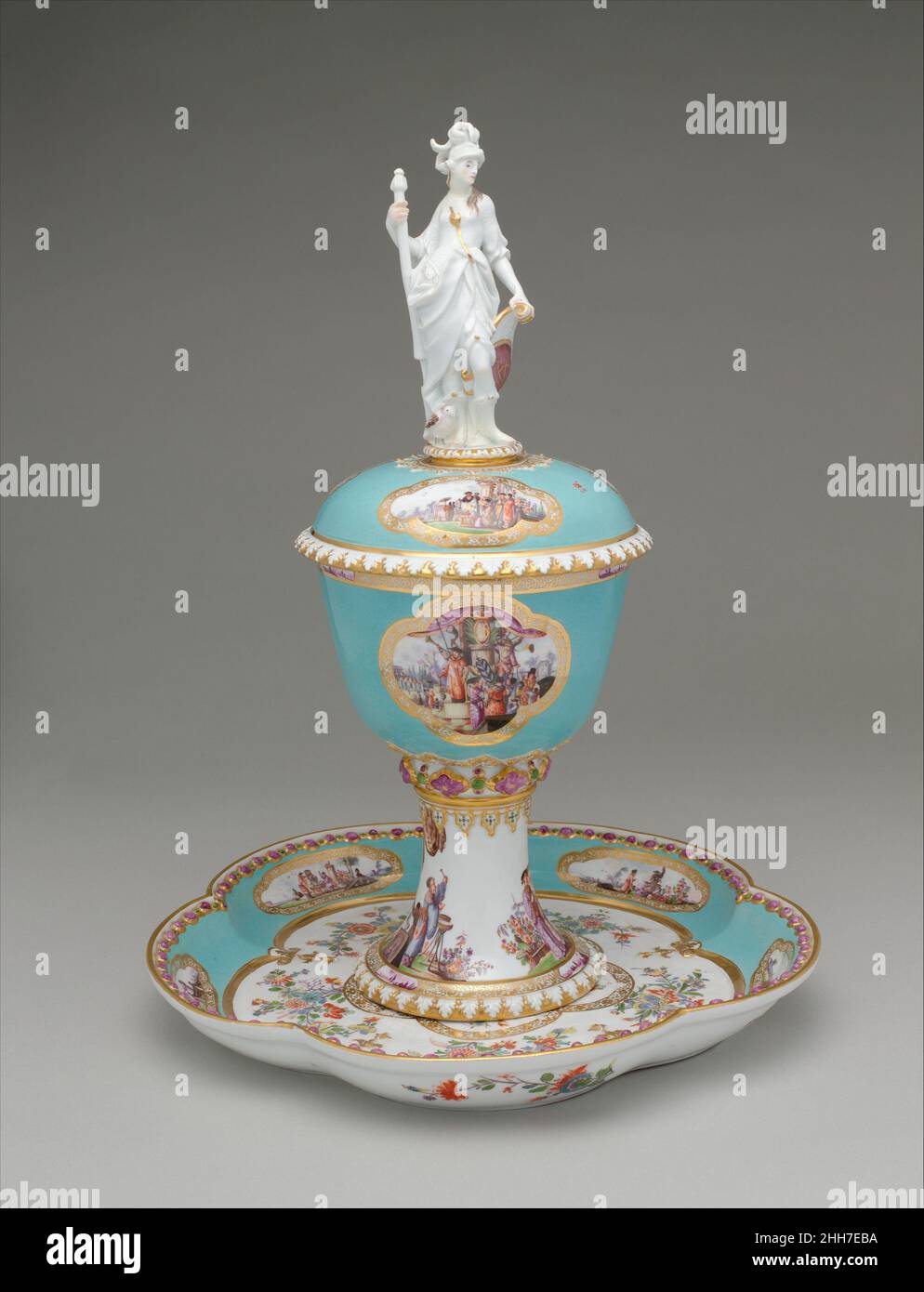 Standing cup with cover and stand ca. 1735 Meissen Manufactory German Commissioned by Augustus the Strong, Elector of Saxony and King of Poland, to commemorate the state visit to Dresden in January 1728 of the king and queen of Prussia, parents of Frederick the Great. The queen’s initials, SD for Sophie-Dorothea, are three times displayed. The larger finial figure of Athena is closely related to a silver statuette in the Electoral collections at Dresden, made by Philipp Kuesel of Augsburg before 1700. The turquoise ground has reserves with gold-lace borders painted by Heroldt with colorful chi Stock Photo