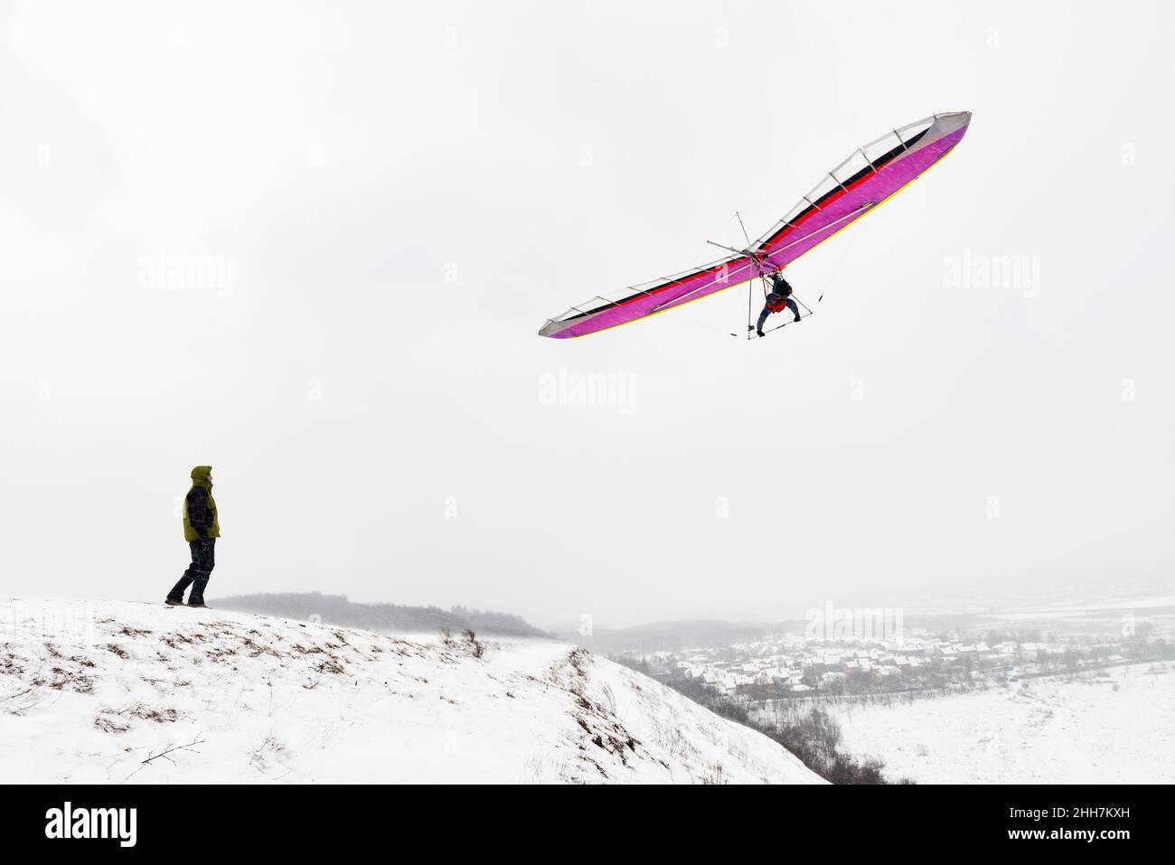 Dream of flying. Man on the hill looks at the flying hang glider wing. Stock Photo