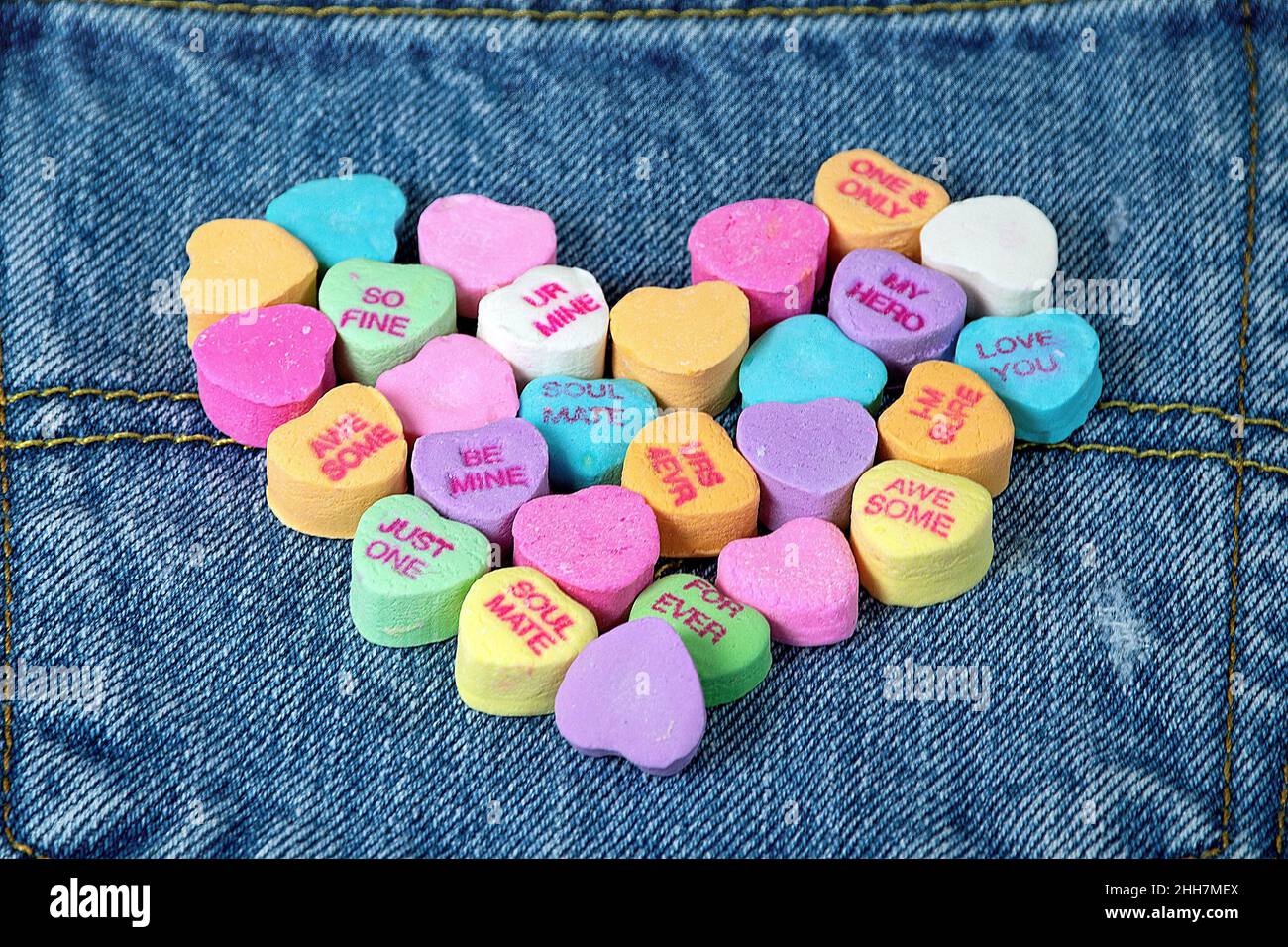 Valentine candy hearts in a heart shape on blue denim fabric Stock Photo