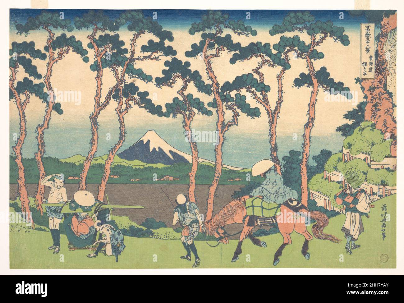 Hodogaya on the Tōkaidō (Tōkaidō Hodogaya), from the series Thirty-six Views of Mount Fuji (Fugaku sanjūrokkei) ca. 1830–32 Katsushika Hokusai Japanese Mount Fuji is enclosed by old pine trees that were planted along the highway as shade and shelter for the travelers. The location of this scene is probably the Gondazaka and Shinanozaka, hills that border the Musashi and Sagami provinces. Palanquin bearers at the left are resting after having crossed the hill. The trappings of the horse carry the trademark of the publisher and the character ju from the publisher's name of Eijudo.. Hodogaya on t Stock Photo