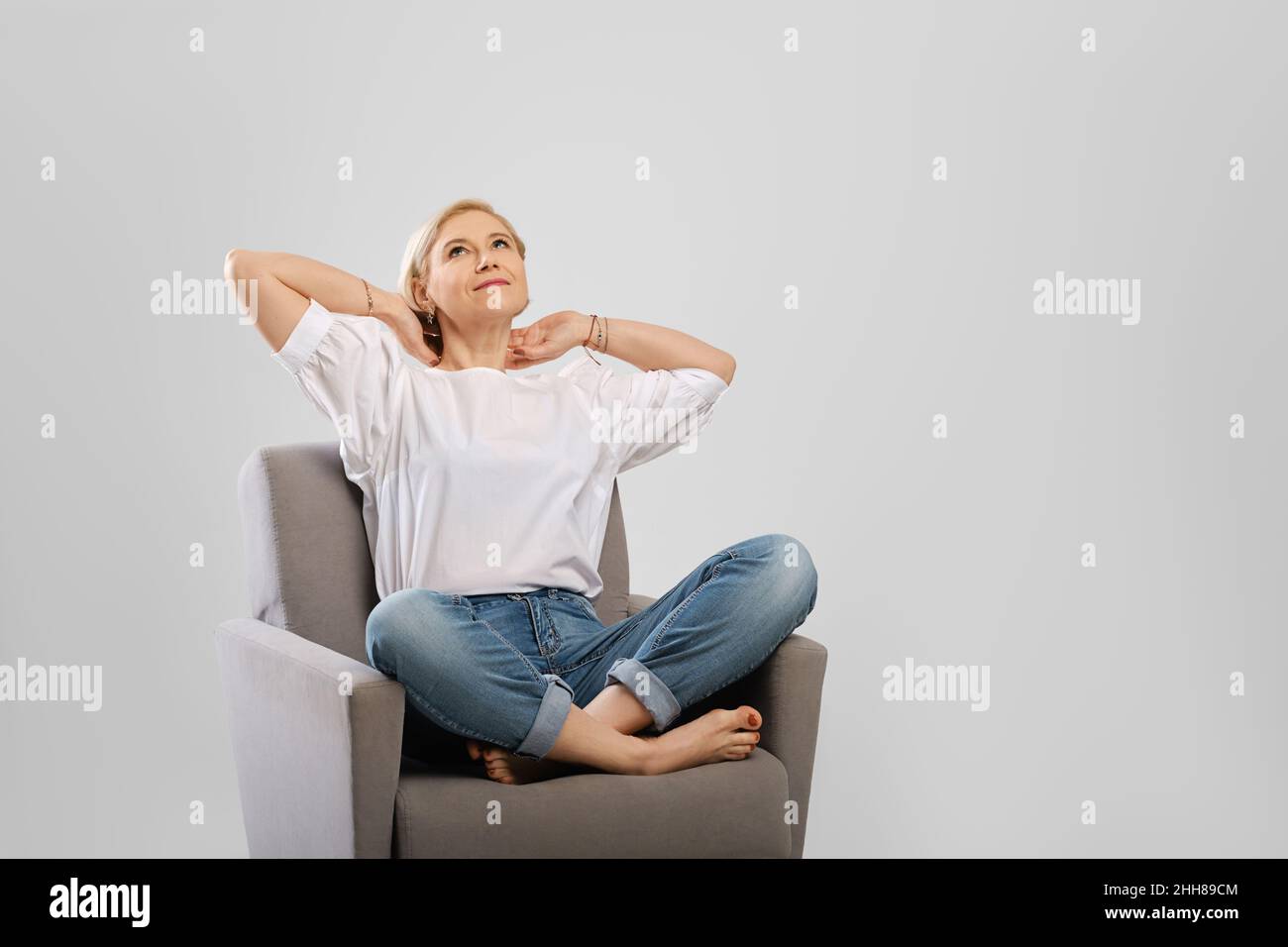 Senior woman relaxing in an armchair crossing legs and hold hands behind her head Stock Photo