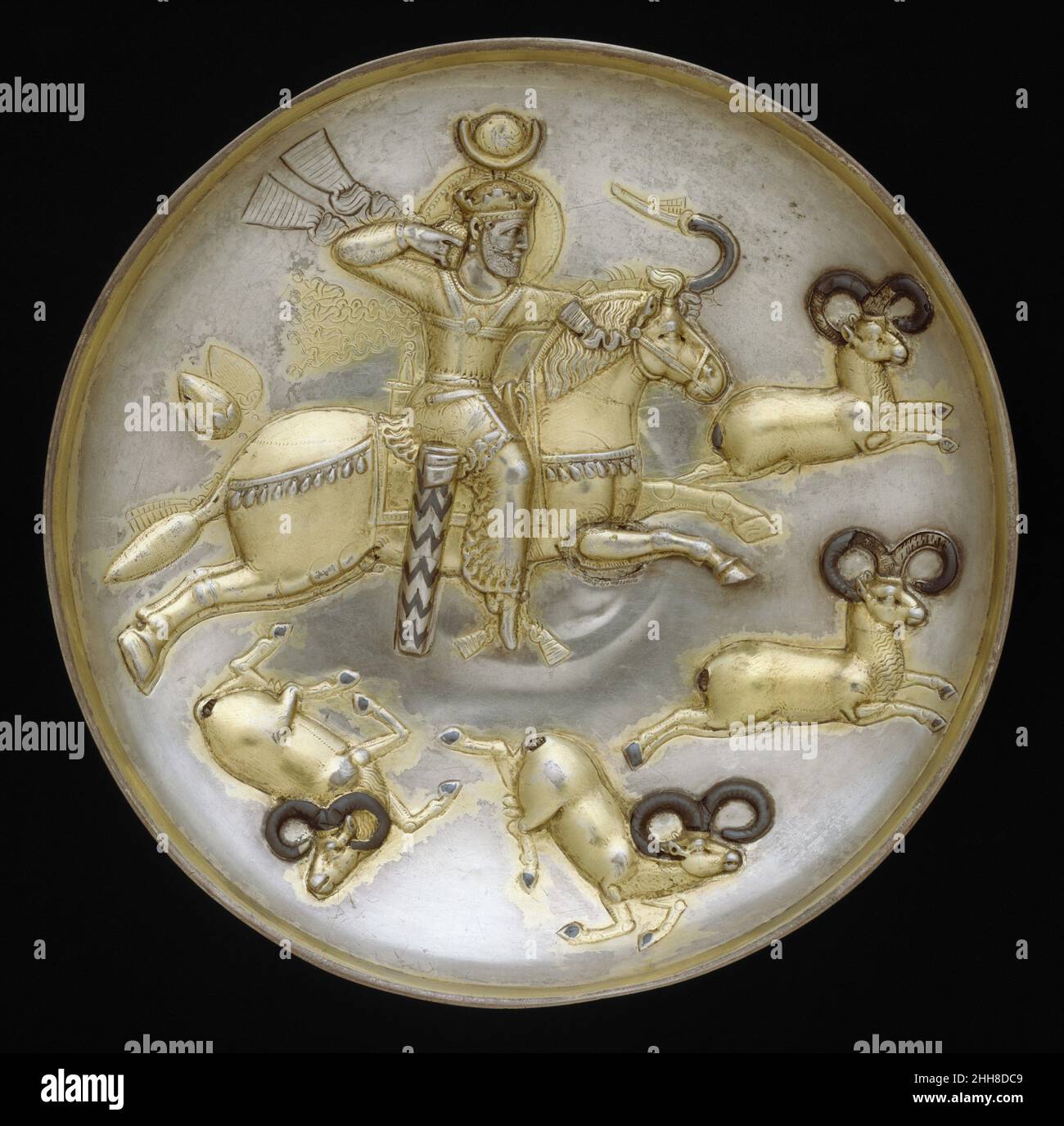 Plate with king hunting rams ca. A.D. mid-5th–mid-6th century Sasanian The king as hunter had become a standard royal image on silver plates during the reign of Shapur II (A.D. 310–379). The theme, symbolizing the prowess of Sasanian rulers, was used to decorate these royal plates, which were often sent as gifts to neighboring courts. The king has various royal attributes: a crown and fillet, covered globe, nimbus with beaded border, and beaded chest halter with fluttering ribbons. The identity of the Sasanian king on this plate is uncertain. His crown identifies him as either Peroz (r. 459–48 Stock Photo