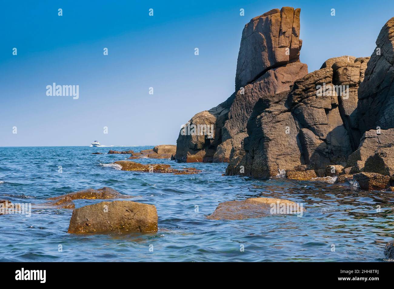Rocky seashore against the blue sky and motor boat on the horizon. Nessebar. Bulgaria Stock Photo