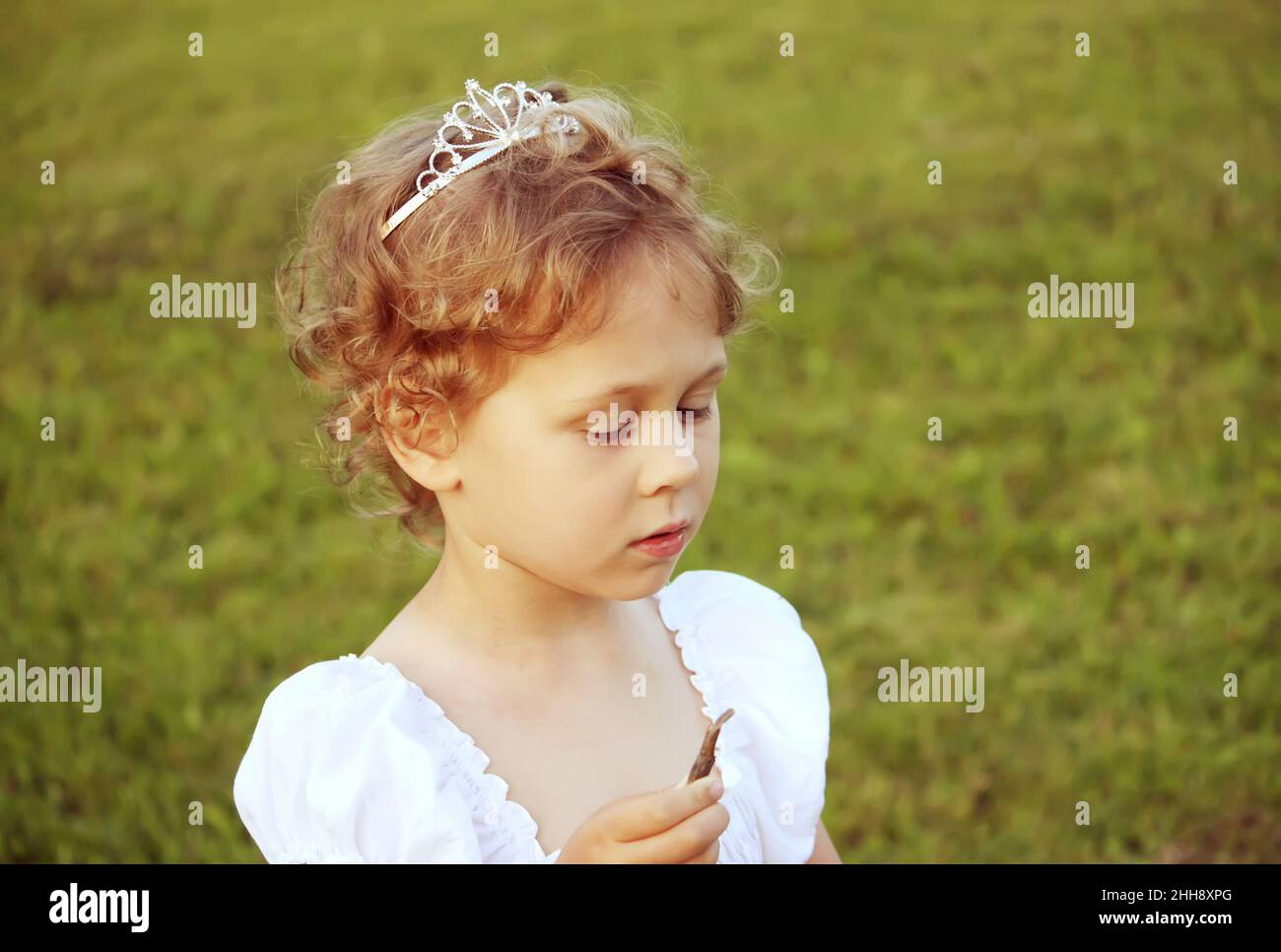 Little girl in white dress with a crown on her head walking outdoors on ...