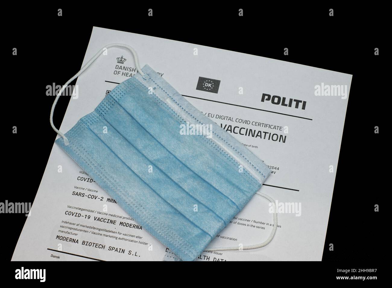 certificate of vaccination issued by the danish Ministry of Health and a blue face mask , Denmark, January 23, 2022 Stock Photo