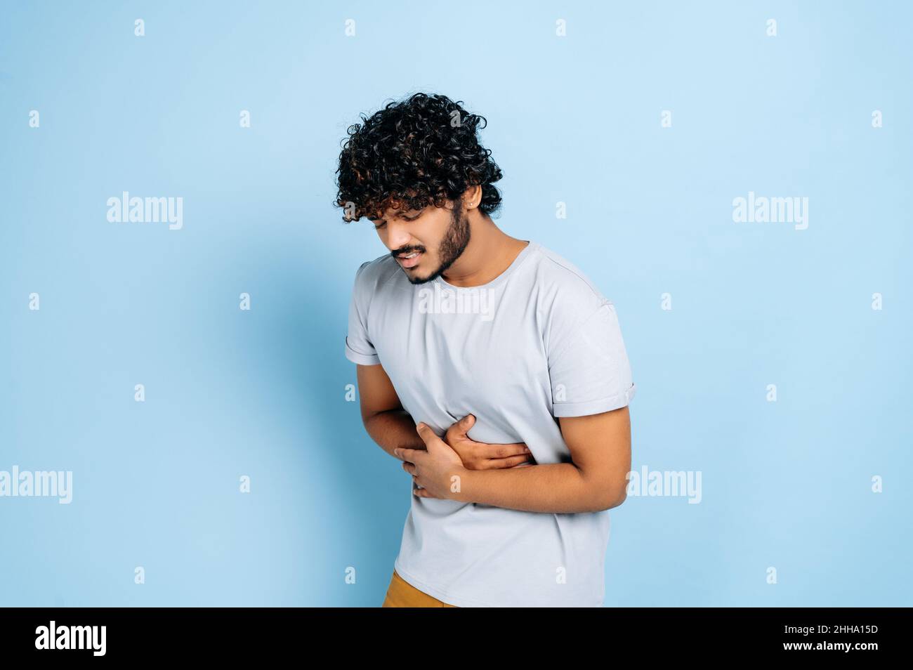 Stomach ache. Indian guy with in casual clothes hunching and holding