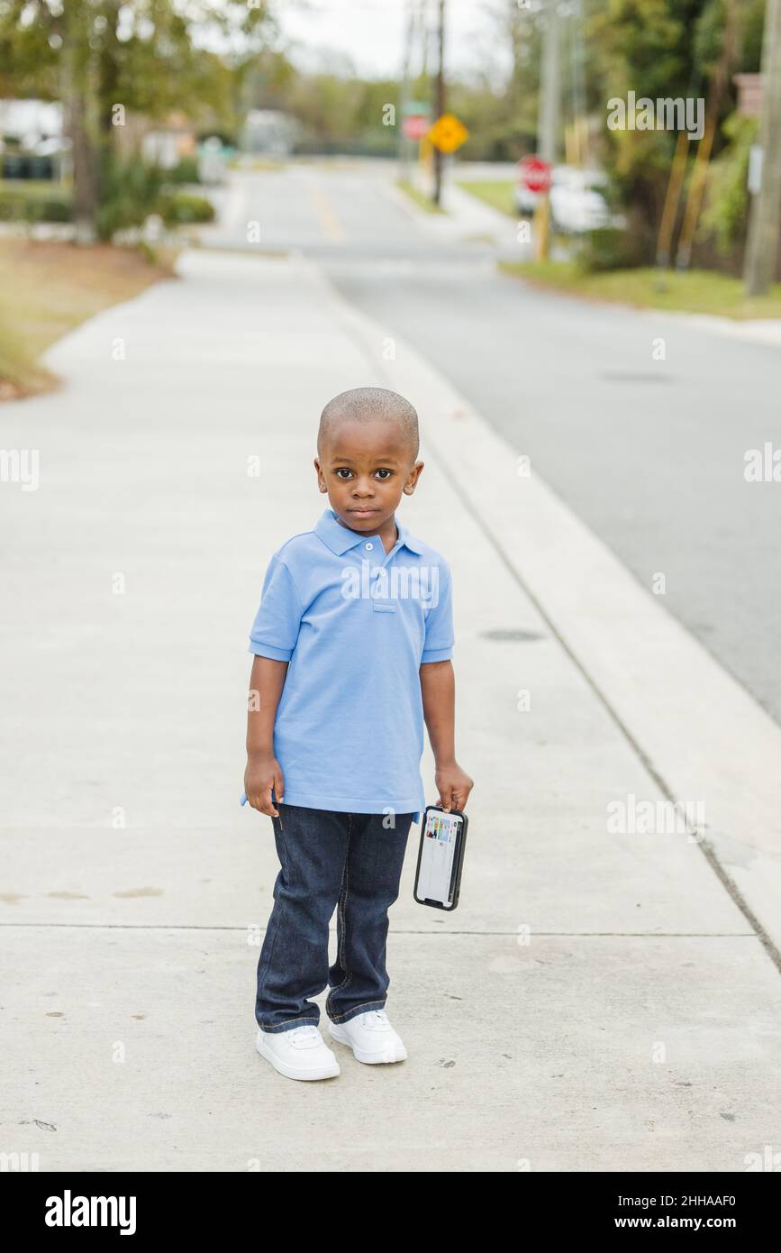 A little boy standing outside holding a cell phone and looking sad Stock Photo