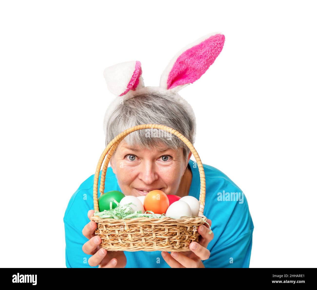 Senior woman peeking out from behind a basket with Easter eggs Isolated on white background Stock Photo