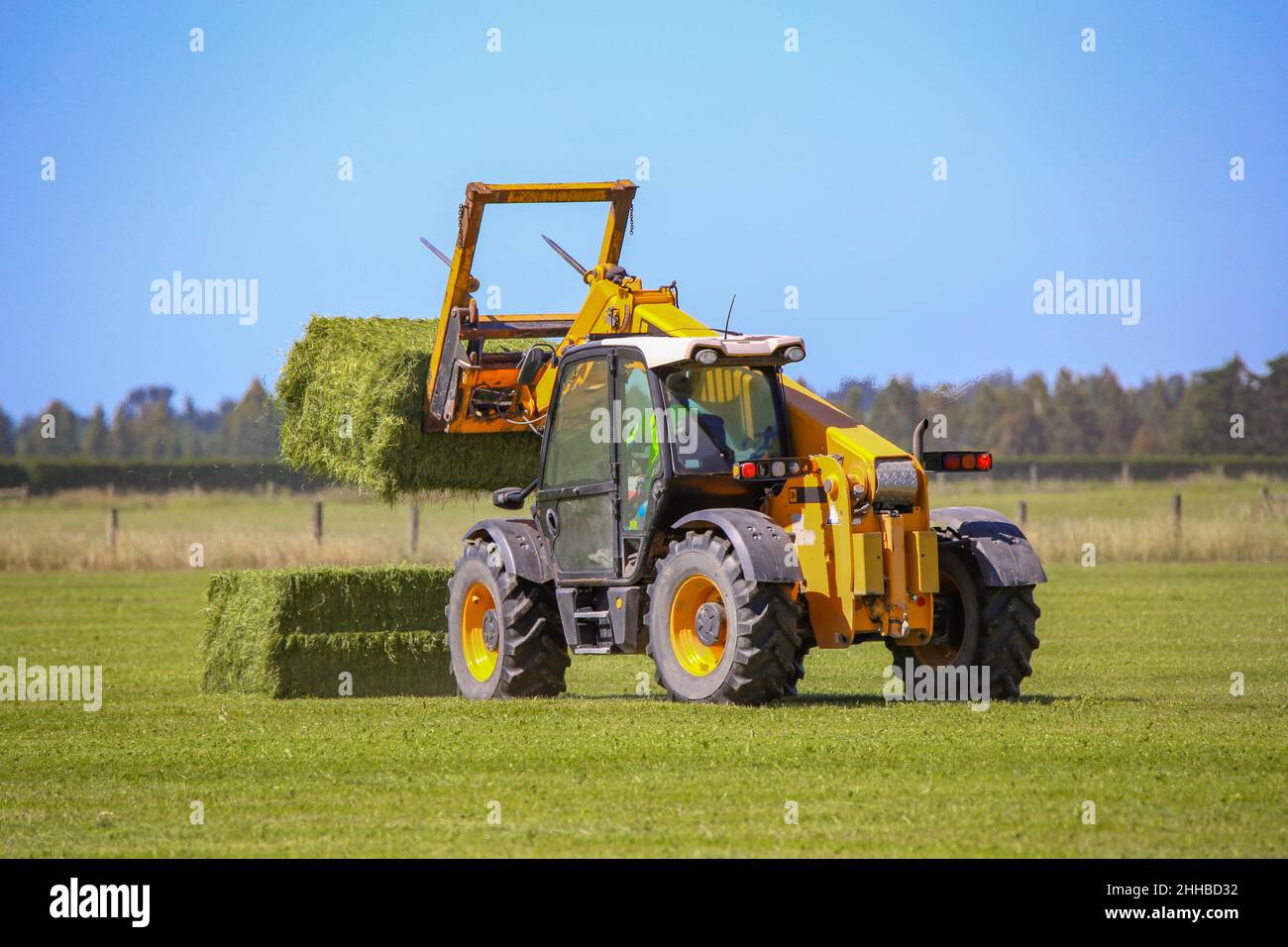 A telehandler works stacking hay bales on a farm in rural Canterbury, New Zealand Stock Photo