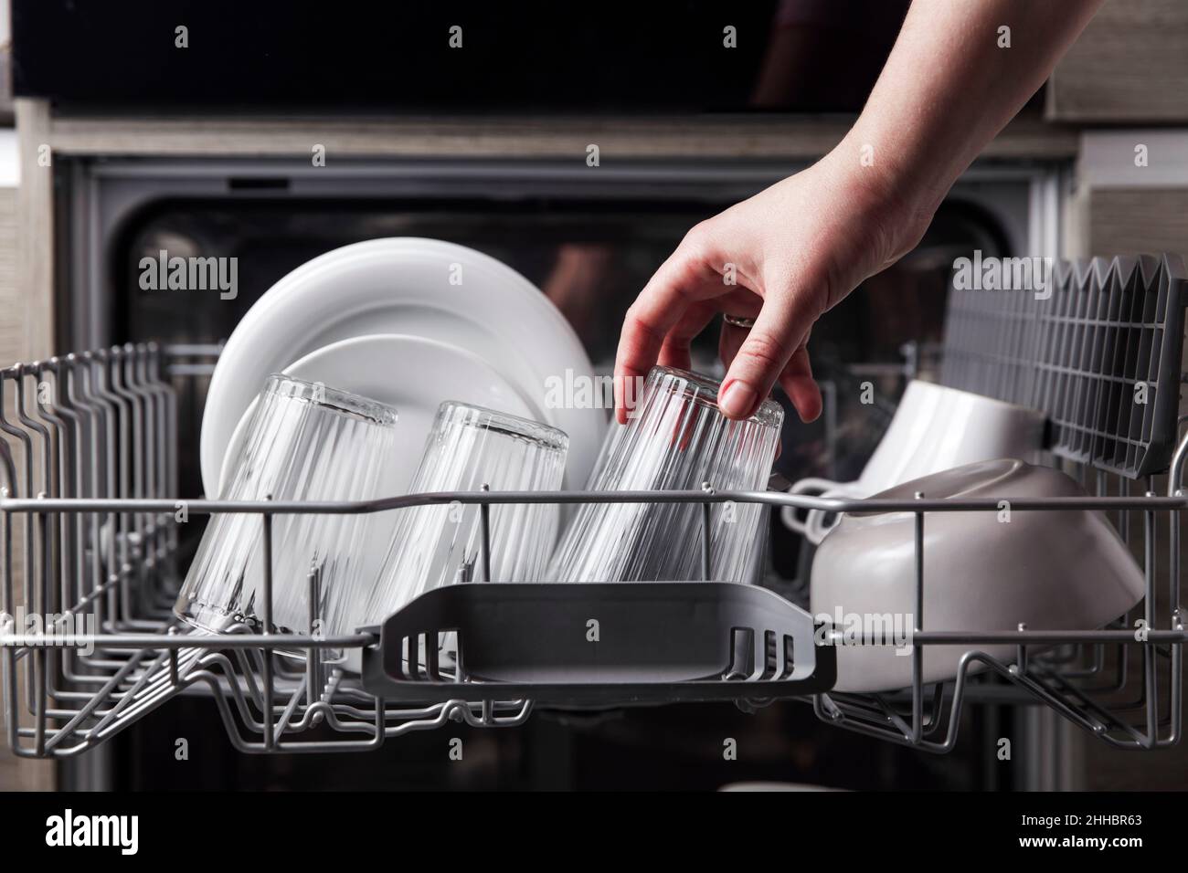 Close-up of female hand loading dished to, empty out or unloading from open  automatic stainless built-in dishwasher machine with clean utensils inside  in modern home kitchen. Household domestic life Stock Photo -