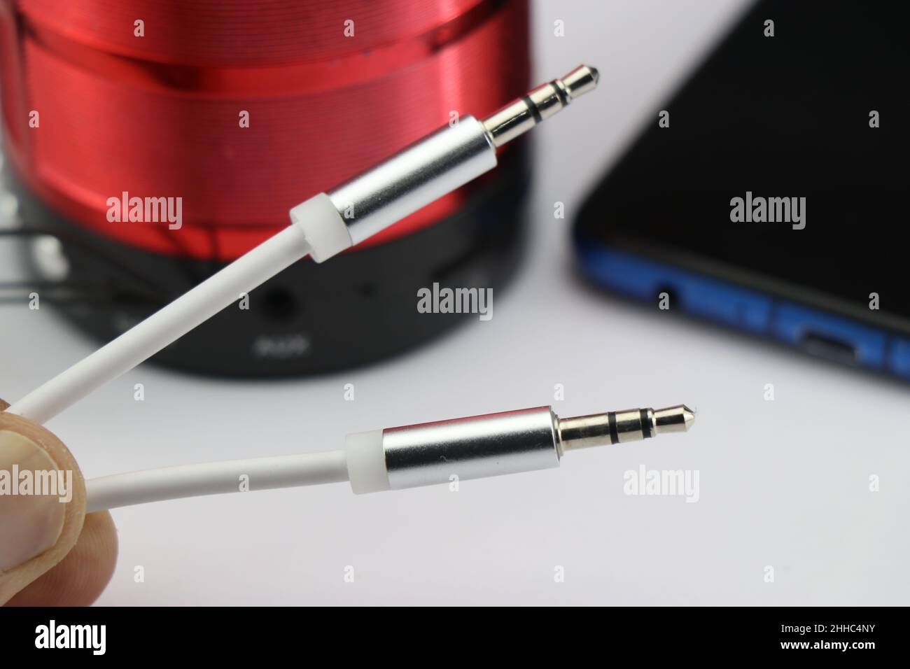 Aux cable or close-up of silver 3.5mm audio jack cable with the smartphone and external speaker on the background. Home Music concept Stock Photo