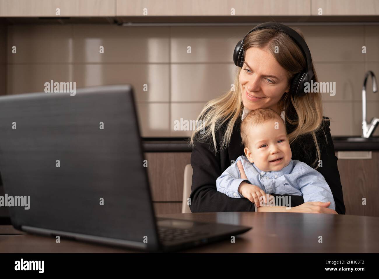 Beautiful mom with baby working remotely with laptop at home, talking