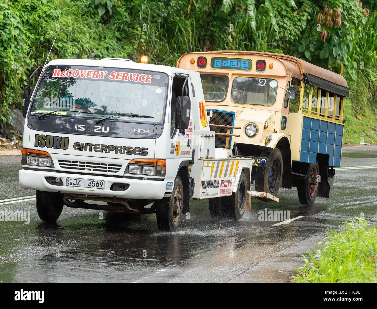 Recovery truck towing a broken down local bus up a hill on a rainy day near Kandy in Sri Lanka. Stock Photo