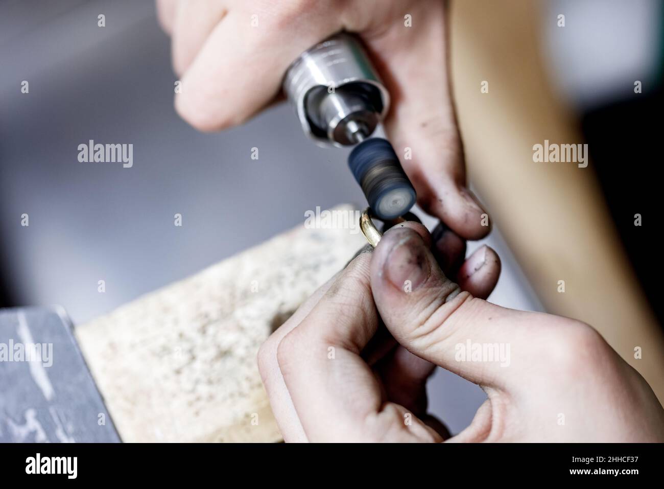 Closeup hands of craftsman jeweler polishing a golden ring surface with grinding machine. Goldsmith is in process of working. Stock Photo