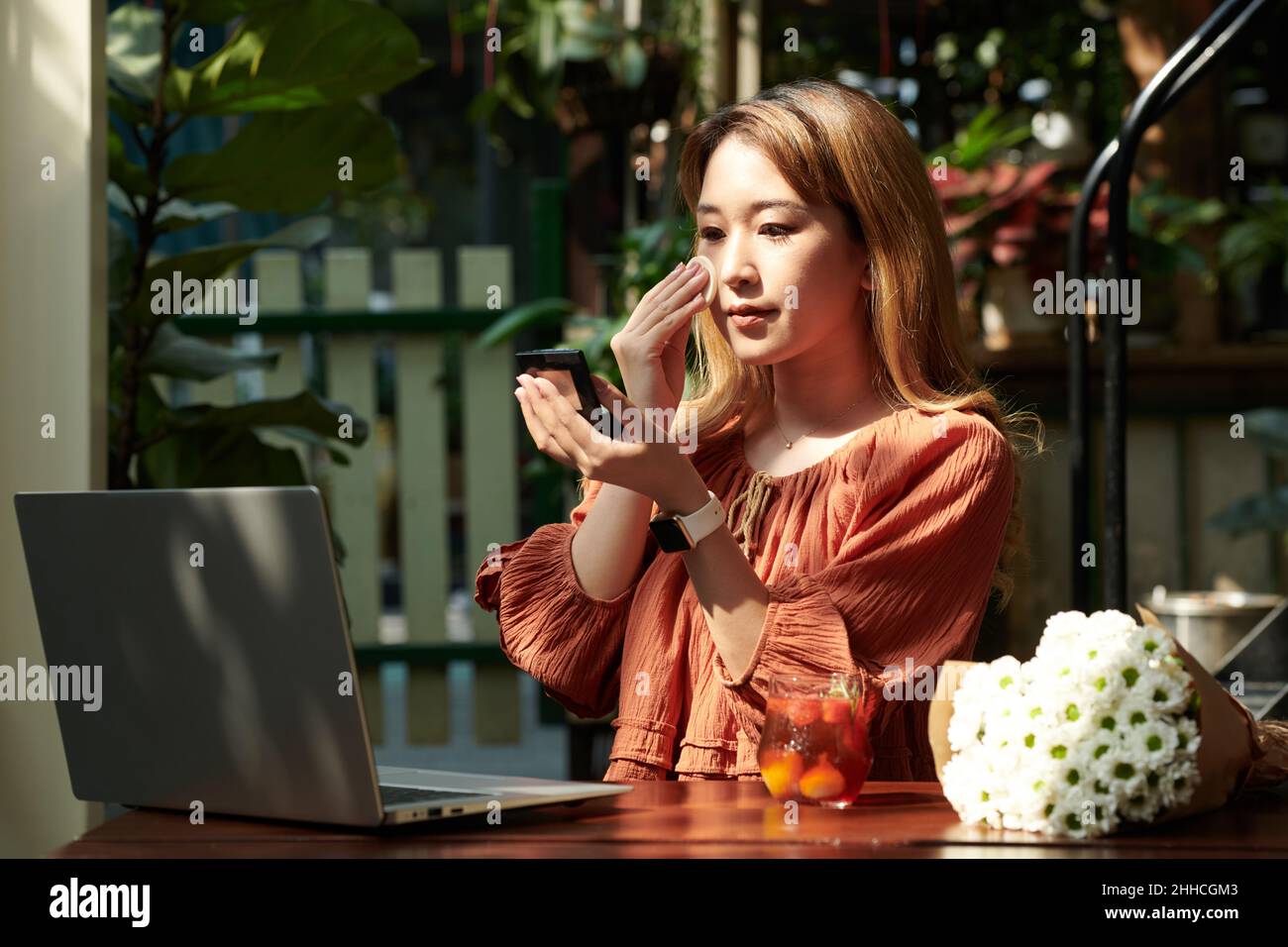Serious young woman applying compact powder on her face before online ...