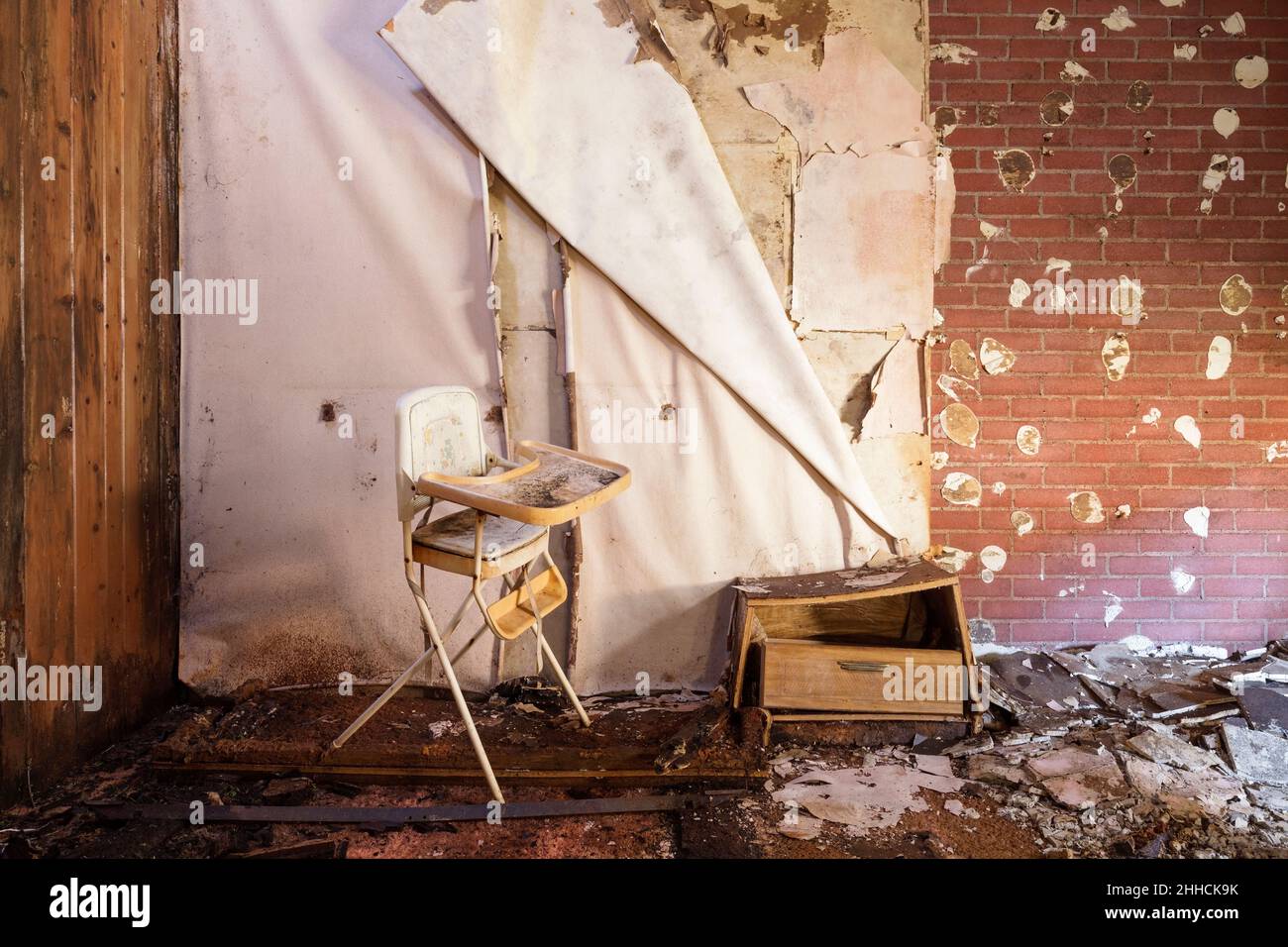 A high chair and a bedside table rotten and falling apart inside an abandoned motel room. Stock Photo