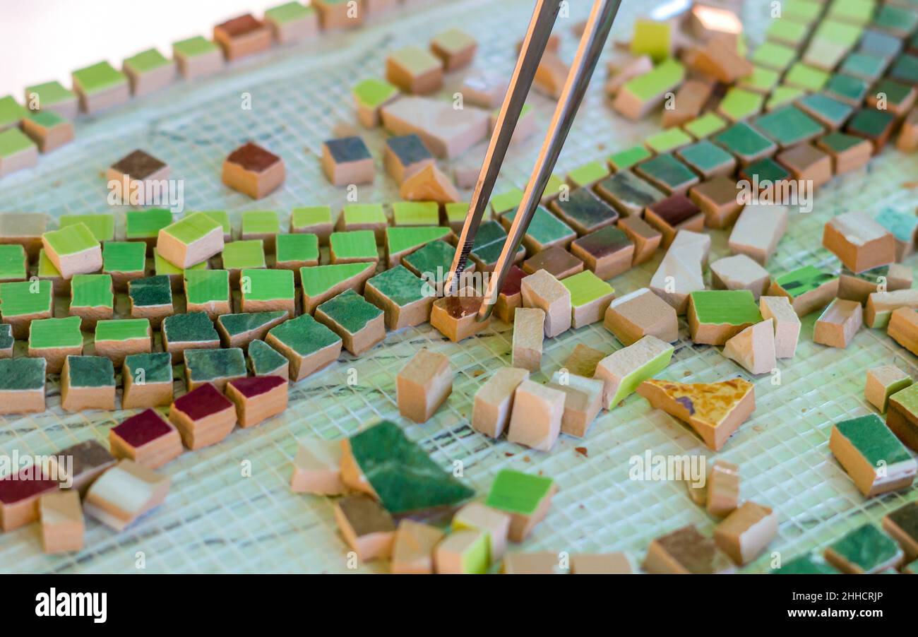 Mosaic as a ceramic or ceramic mosaic. The man organizes design with a tweezers a puzzle of ceramic elements for the construction of ceramic works. Ar Stock Photo